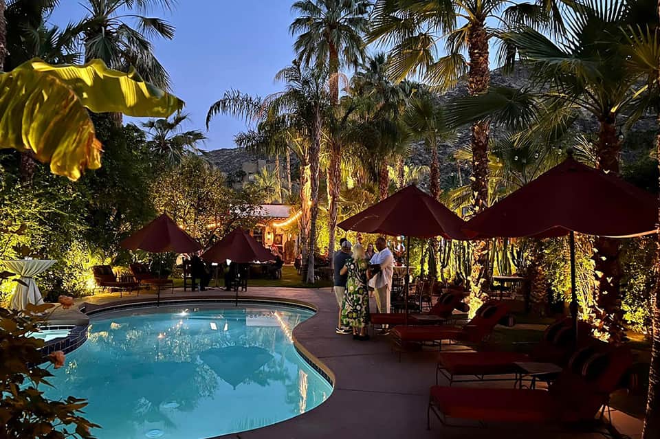 Evening poolside scene with burgundy umbrellas, palm trees, and ambient lighting at desert resort