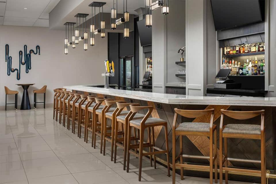 Upscale bar counter with wooden bar stools, pendant lighting, and fully stocked liquor shelves behind