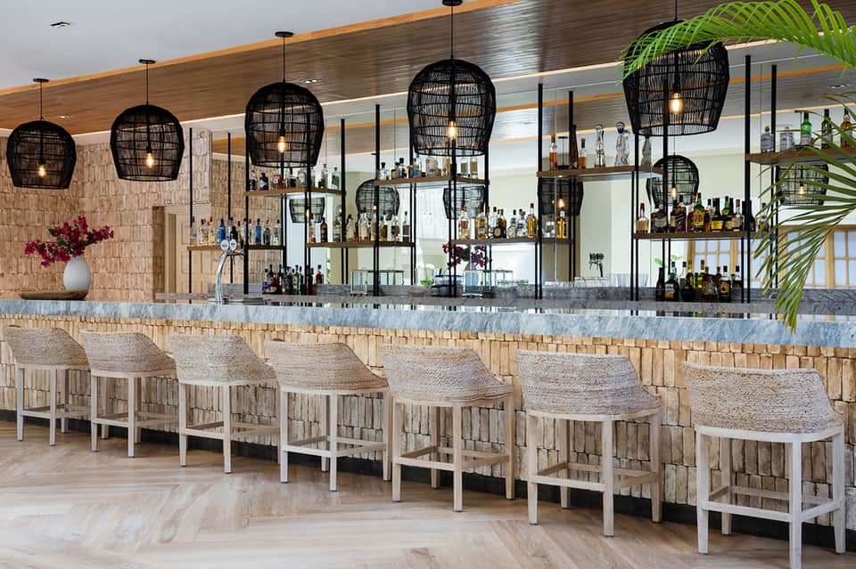 Modern bar with black woven pendant lights, marble counter, and neutral-toned bar stools with wooden base accents