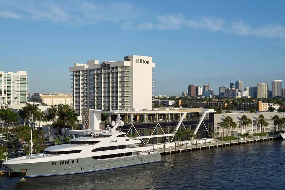 Hilton hotel with luxury yacht docked at riverfront, city skyline in background