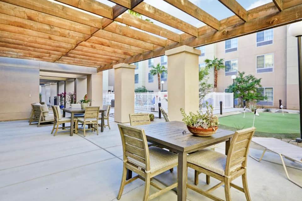 Outdoor covered patio with wooden pergola, dining tables, and view of courtyard with palm trees and manicured lawn