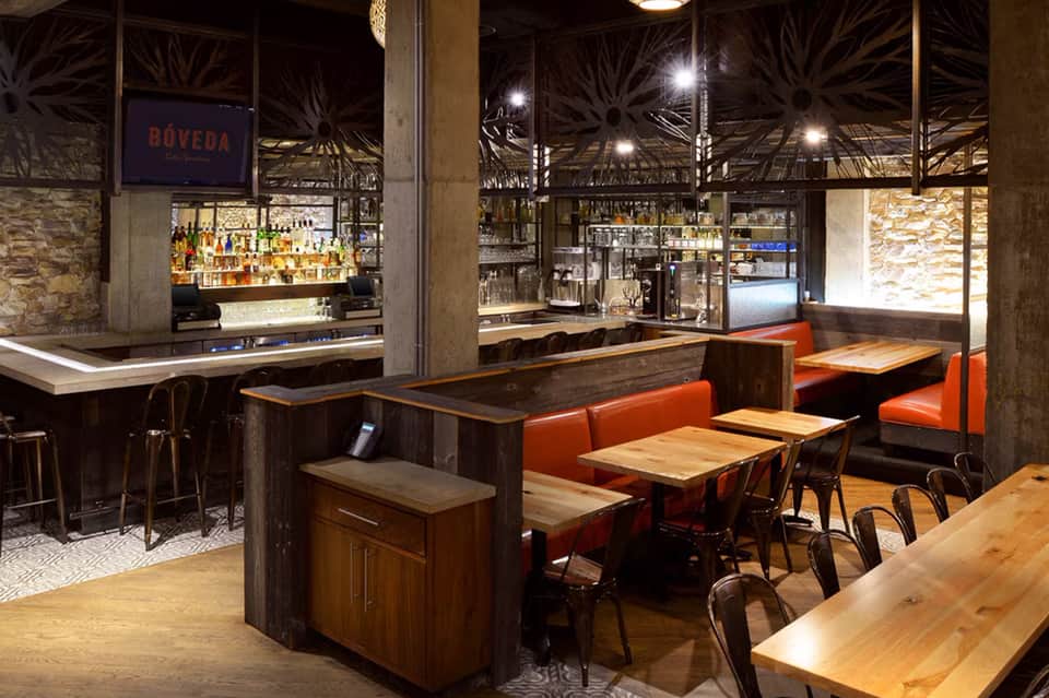 Modern bar and dining area with orange seating, wooden tables, and illuminated palm tree ceiling design
