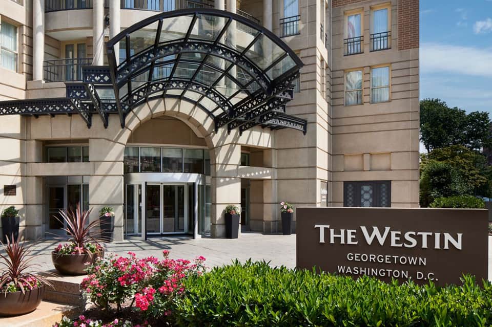 The Westin Georgetown entrance with ornate black awning, stone facade, and pink flowering planters