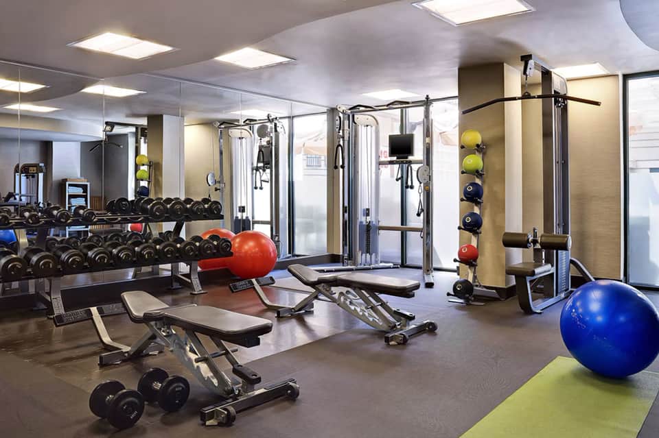 Modern hotel fitness center with dumbbells, exercise machines, stability balls, and glass-walled gym equipment
