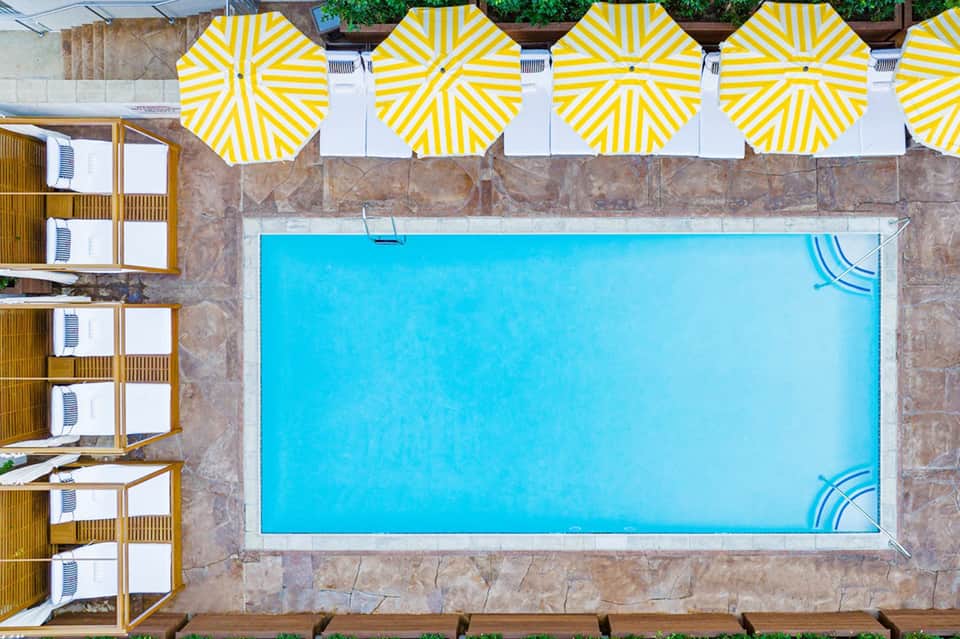 Overhead view of rectangular swimming pool with bright yellow and white striped umbrellas and cabanas