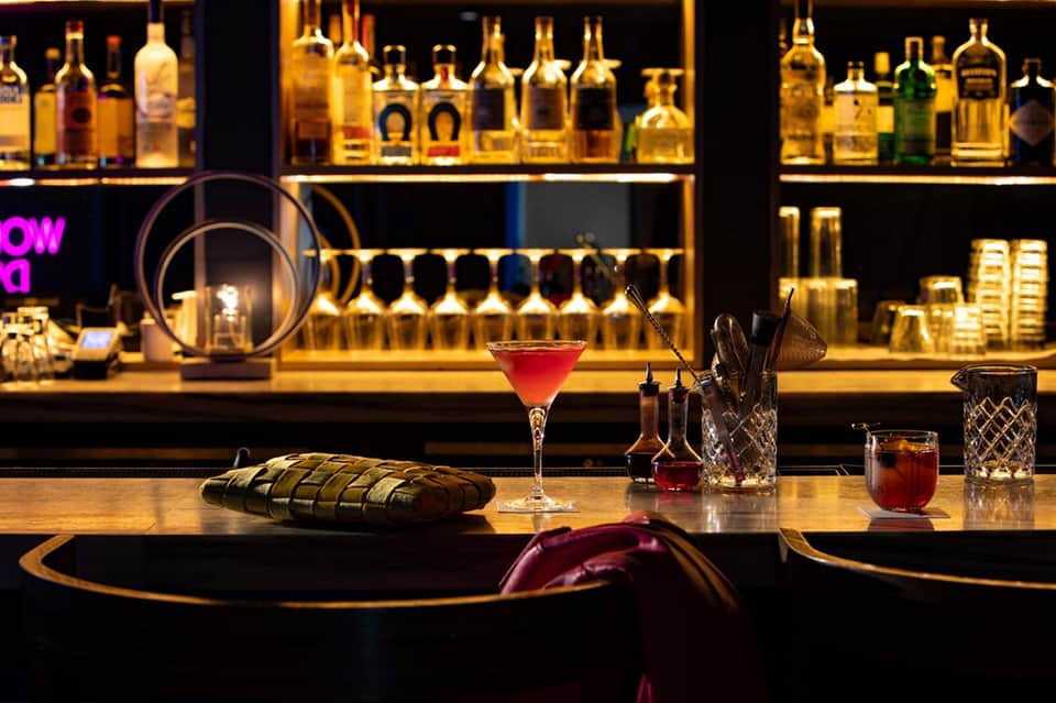 Elegant bar counter with red cocktail and illuminated bottle display shelves in background