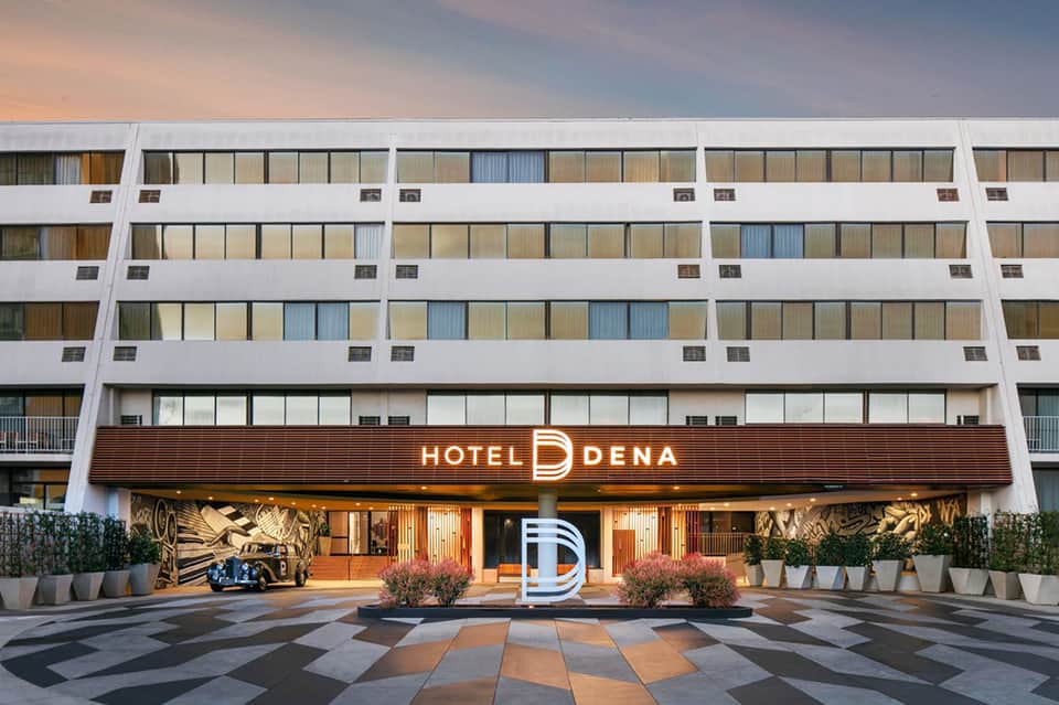 Hotel Dena modern entrance with illuminated signage, geometric patterned courtyard, and residential tower above at dusk