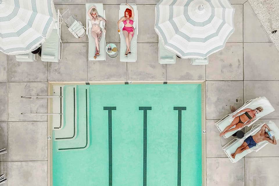 Aerial view of resort pool with guests sunbathing on loungers and under umbrellas