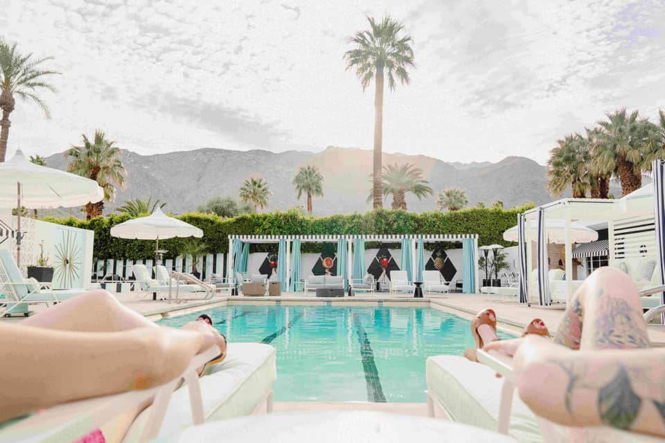 Turquoise resort pool with lounge chairs, cabanas, and palm trees against desert mountains