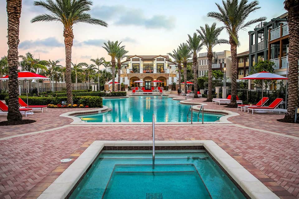 Resort pool area with red umbrellas, spa building, and palm trees in tropical setting