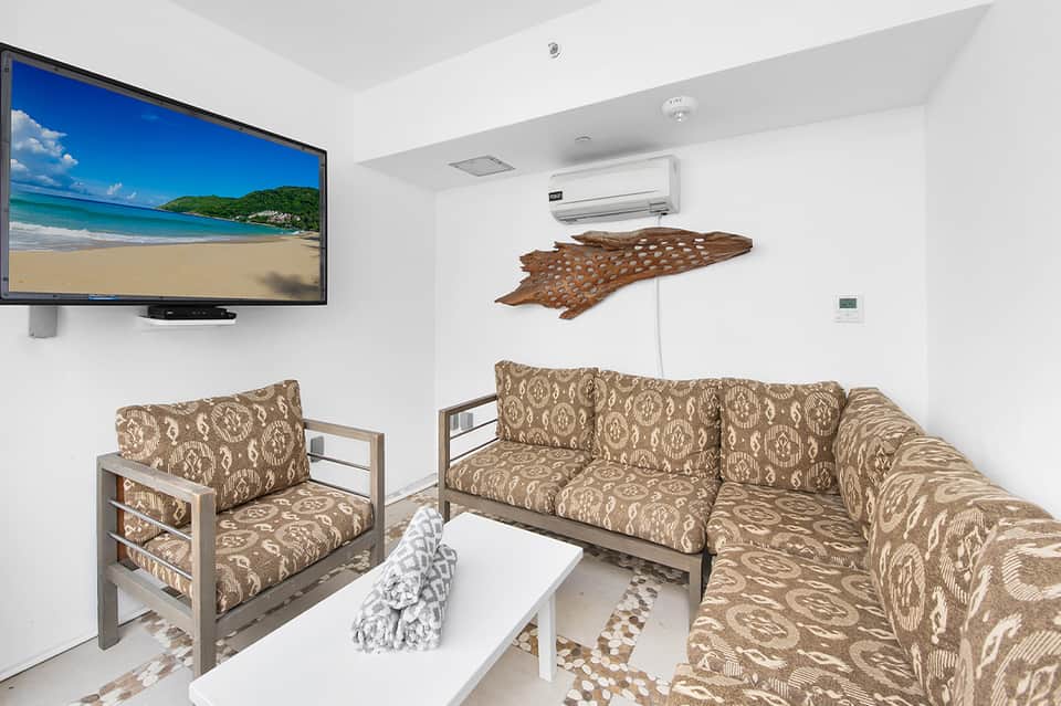 Relaxation room with patterned seating, wall-mounted TV showing beach scene, and air conditioning