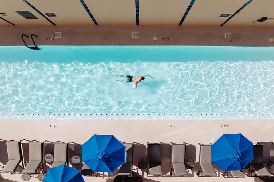 Overhead view of Olympic swimming pool with swimmer doing freestyle stroke and blue umbrellas on deck