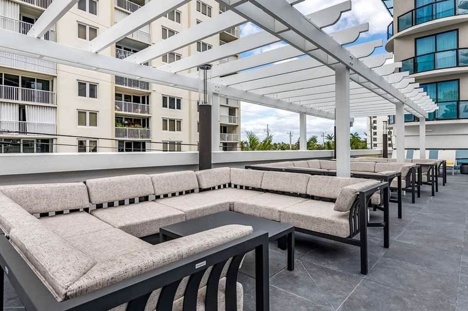 Modern rooftop terrace with sectional seating, fire pit, pergola structure, and city views