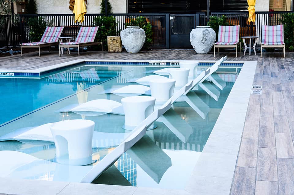 Resort pool with white lounge chairs, pink striped deck chairs, and decorative white planters
