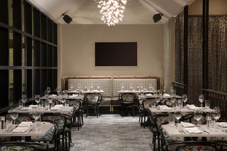 Elegant dining room with long tables, patterned chairs, beige banquette seating, and modern chandelier