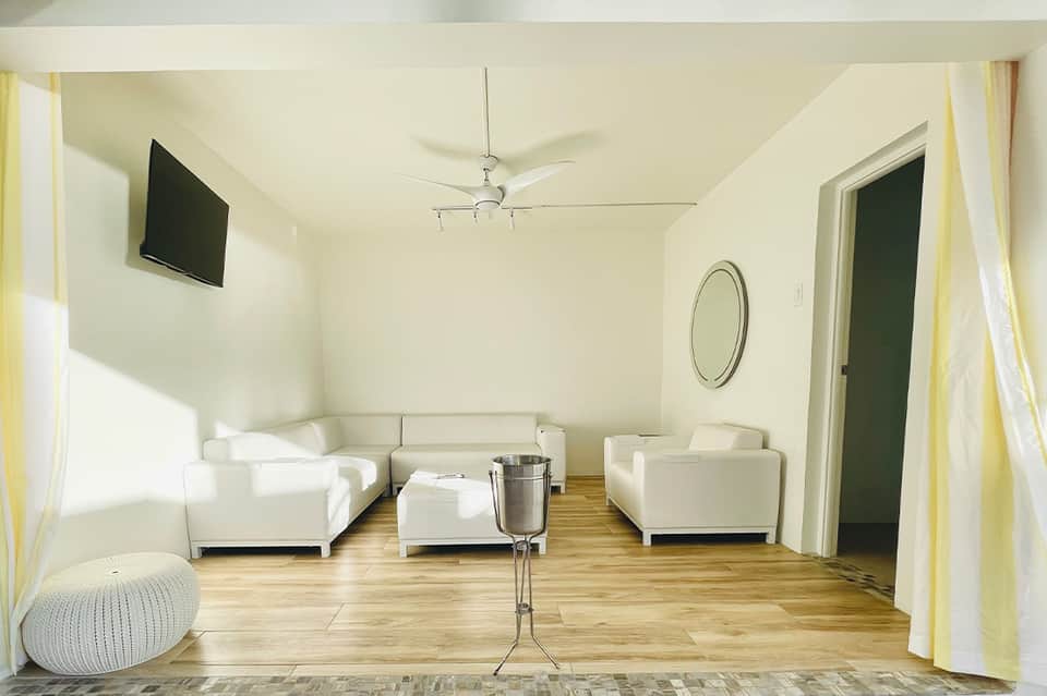 Modern lounge with white sofas, wooden floor, ceiling fan, and minimalist décor