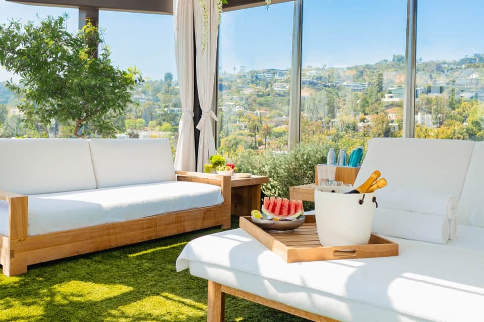 Luxury hilltop terrace with wooden loungers, white cushions, and panoramic city views through floor-to-ceiling windows