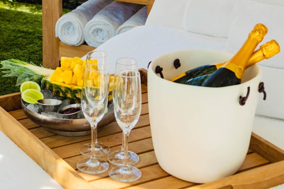 Poolside champagne service with flute glasses, ice bucket, fresh pineapple, and rolled towels on wooden table