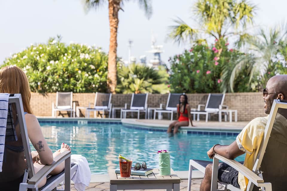 Guests relaxing by resort pool with lounge chairs, tropical landscaping, and palm trees