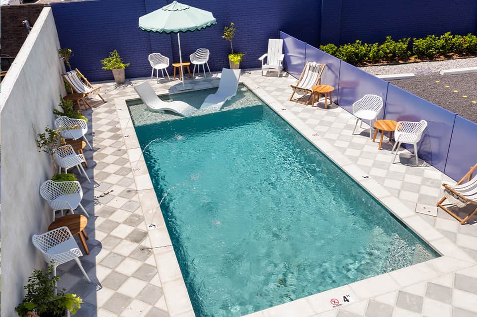 Outdoor pool deck with turquoise lap pool, lounge chairs, umbrellas, and modern white chairs