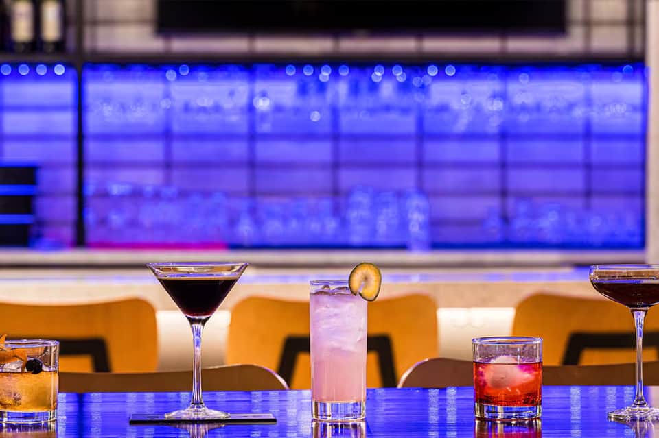 Colorful cocktails on blue bar counter with orange chairs and illuminated blue backdrop