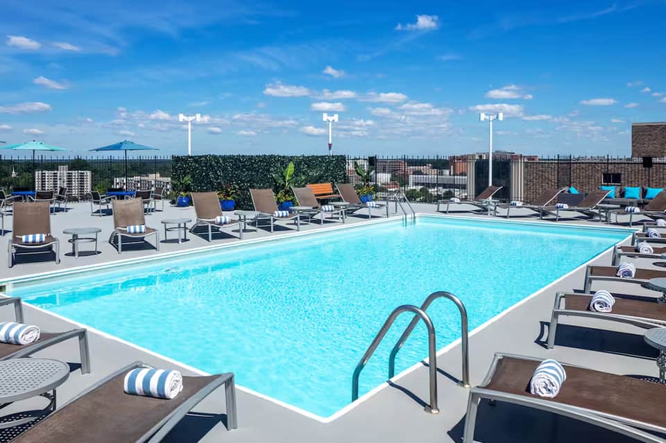 Rooftop pool with bright blue water, lounge chairs, and city skyline views under clear blue sky