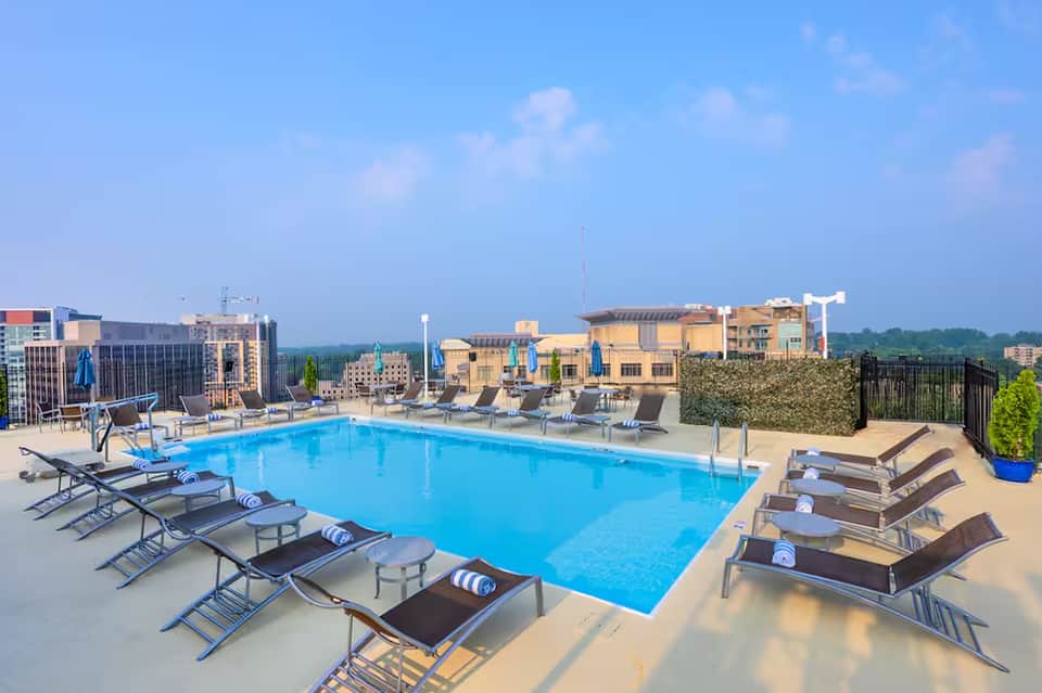 Rooftop pool with blue water, lounge chairs, and city skyline with yellow buildings in background