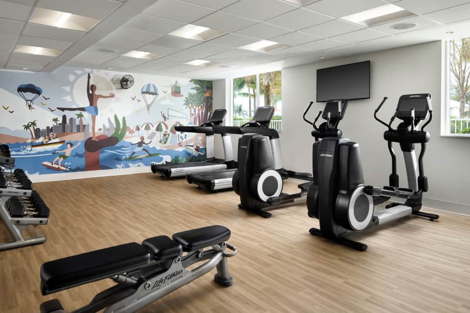 Modern fitness center with cardio equipment, colorful mural, and wooden flooring