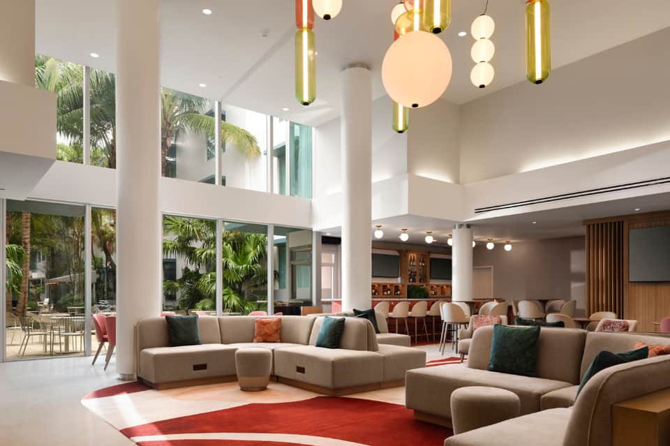 Luxurious lobby lounge with high ceilings, modern pendant lighting, beige seating, and garden views