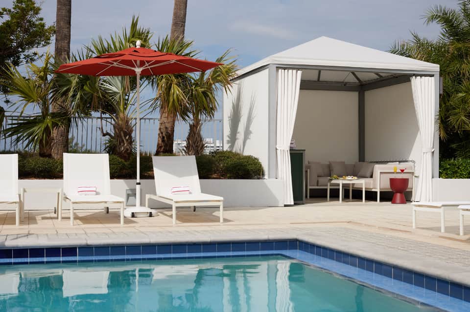 Luxury resort poolside with white cabana, red umbrella, loungers, and palm trees