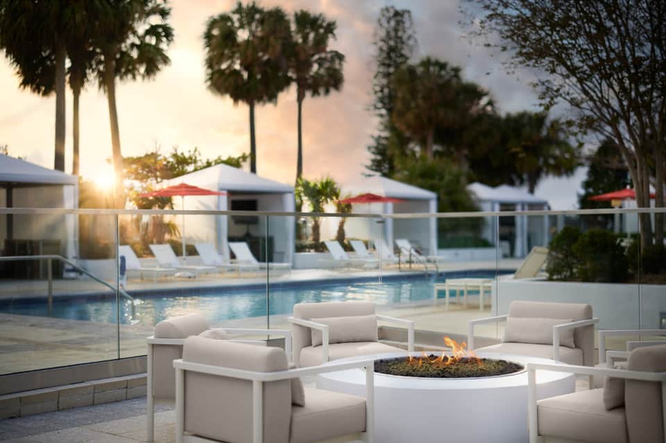 Resort pool at sunset with white fire pit seating, palm trees, and cabanas