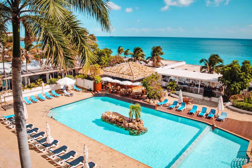 Beachfront resort pool with turquoise water, lounge chairs, palm trees, and ocean views