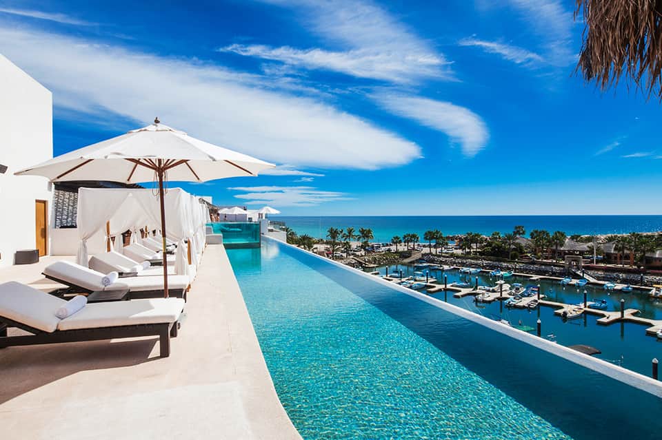 Luxury oceanside infinity pool with white loungers, umbrellas, and coastal marina views