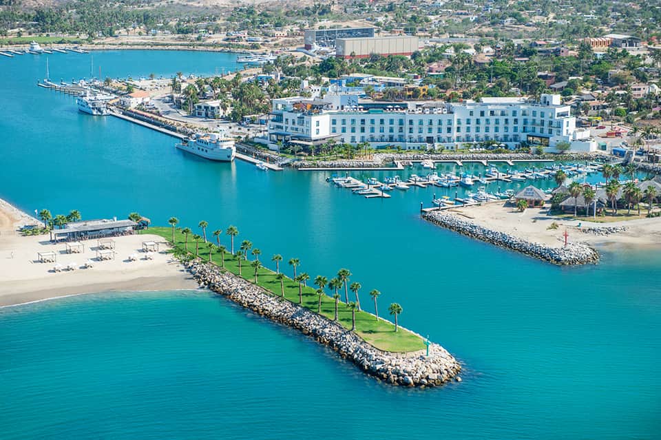 Aerial view of beachfront hotel with white building, cruise ships, marina, and turquoise ocean