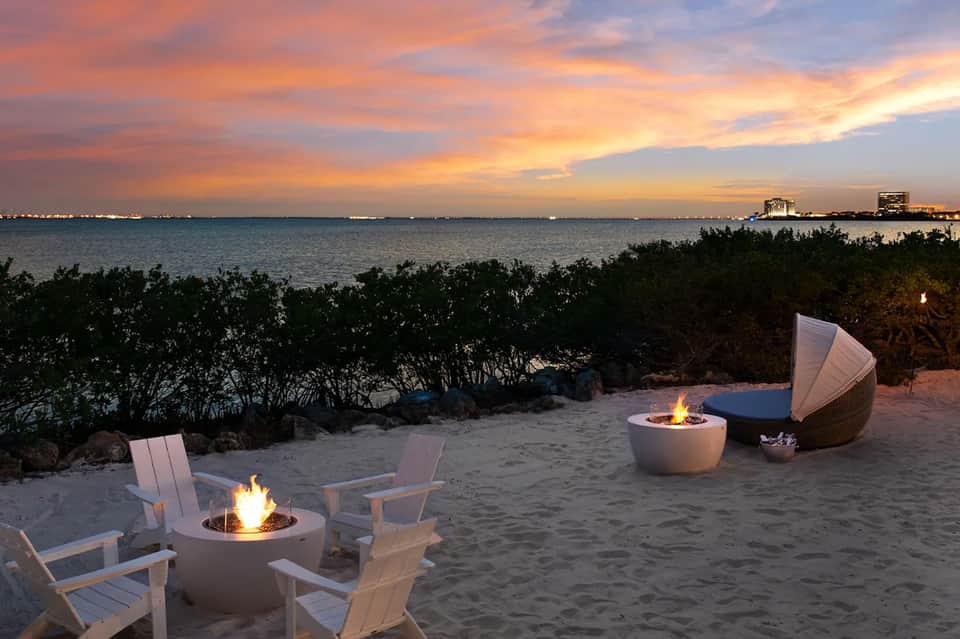 Beach bonfire setup at sunset with white Adirondack chairs and ocean view
