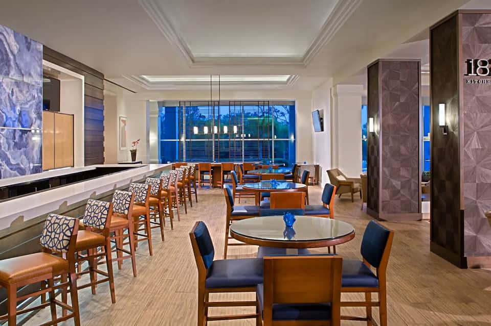 Modern hotel lounge with wooden chairs, blue accents, and panoramic evening city views