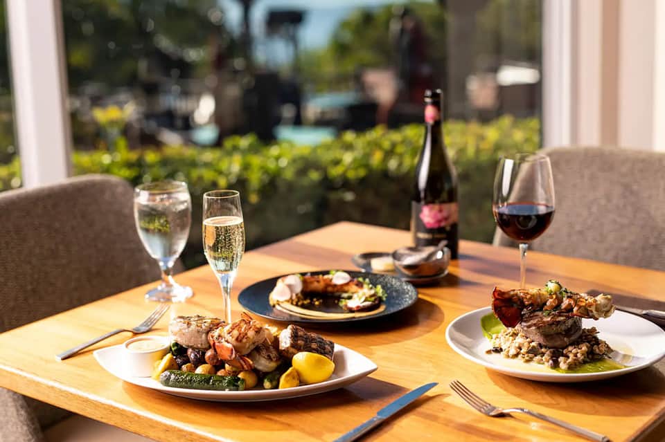 Fine dining table with plated entrees, wine glasses, and ocean garden views