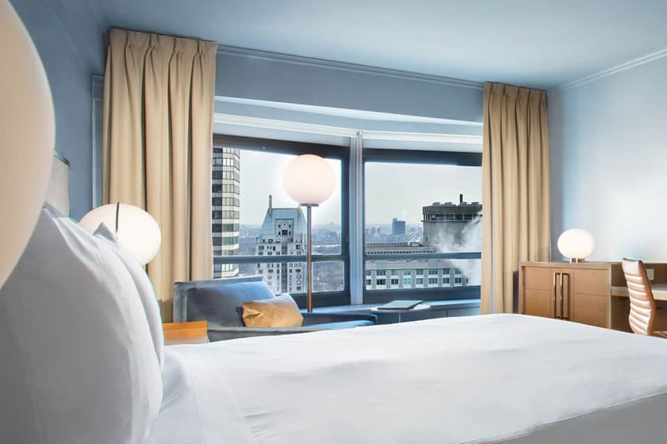 Hotel bedroom with city skyline view through floor-to-ceiling windows