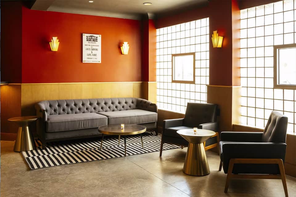 Mid-century modern lounge with red and gold walls, gray tufted sofa, brass side tables, and geometric lighting