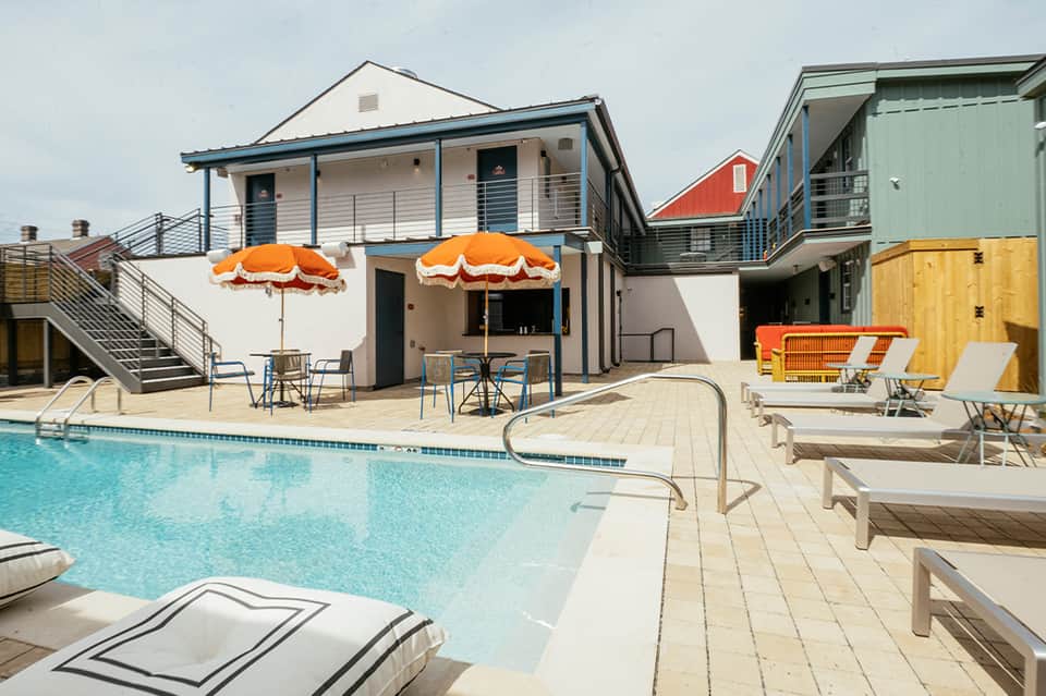Beachfront resort pool with orange umbrellas, modern clubhouse, and waterfront lounge chairs