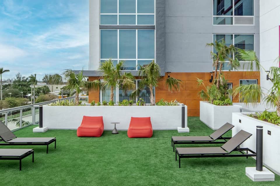Modern rooftop terrace with red bean bag chairs, lounge chairs, and palm trees overlooking city