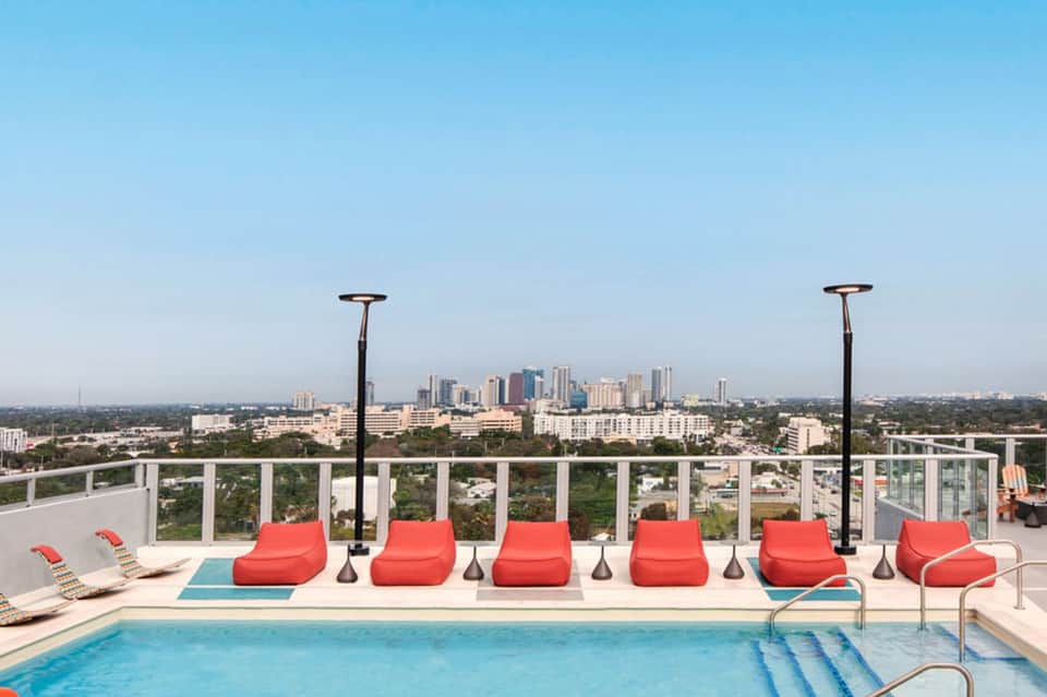 Rooftop pool area with red loungers, heaters, and city skyline view in the distance