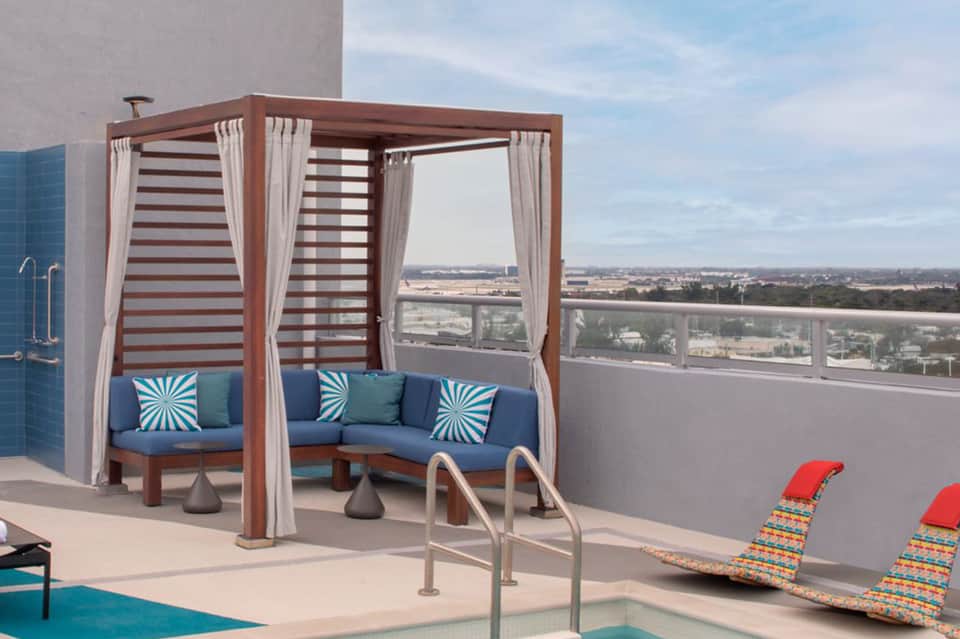 Rooftop lounge with striped cabana, blue seating, and panoramic cityscape views