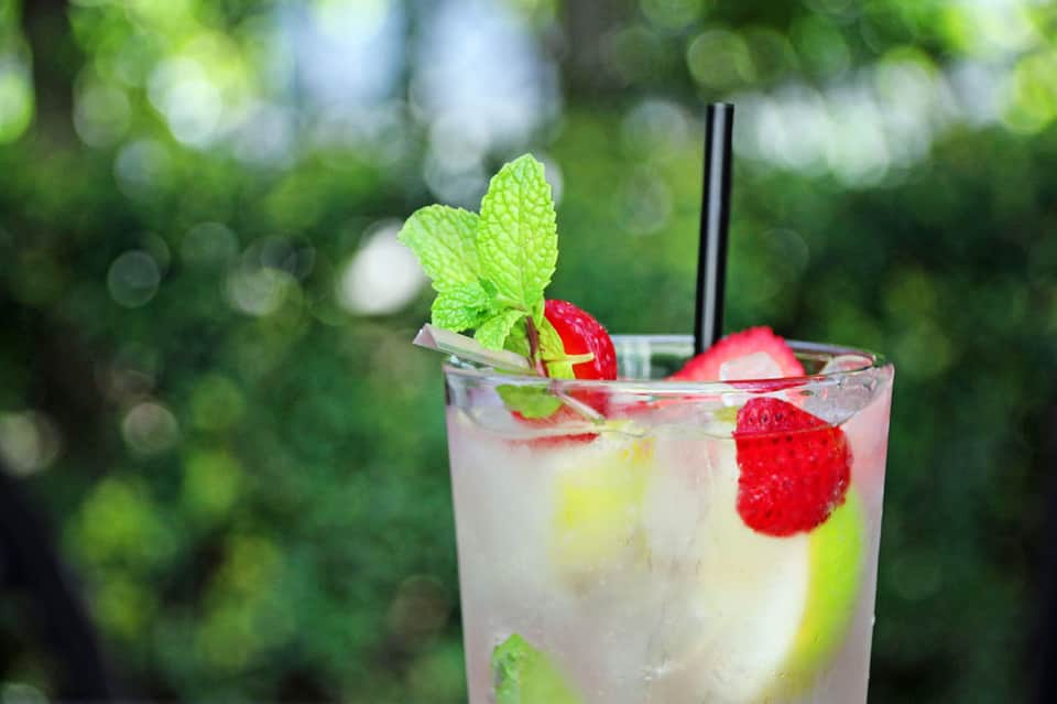 Refreshing cocktail with fresh raspberries and mint leaves garnished with a black straw