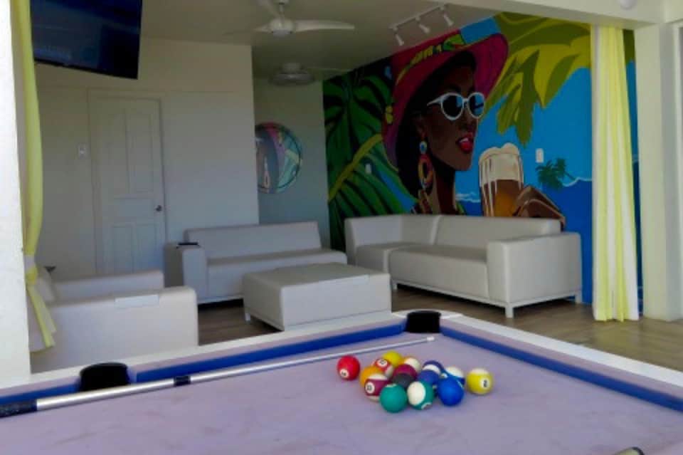 Game room with pool table, white seating, and colorful tropical mural artwork on walls