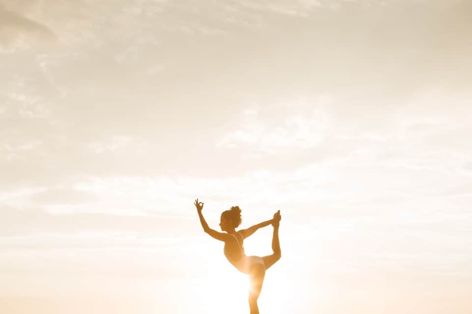 Woman in yoga pose silhouetted against golden sunset sky