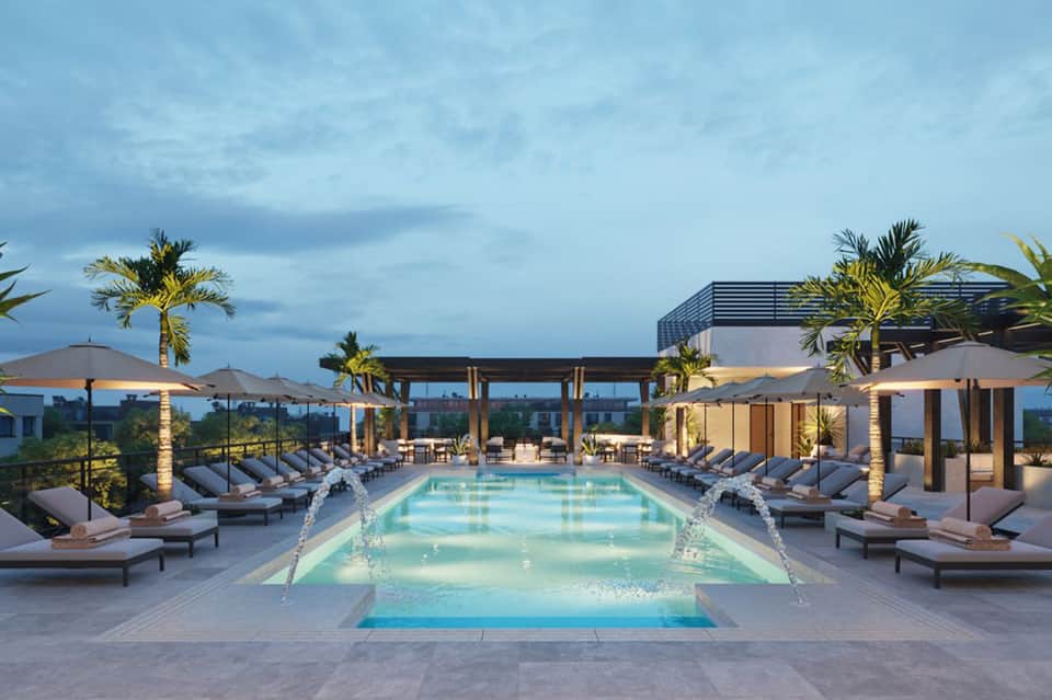 Luxury rooftop pool at dusk with loungers, palm trees, modern architecture, and city skyline views