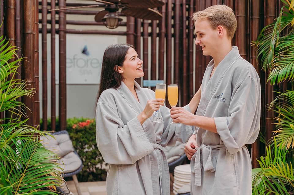 Couple in spa robes toasting with champagne glasses in a tropical courtyard setting