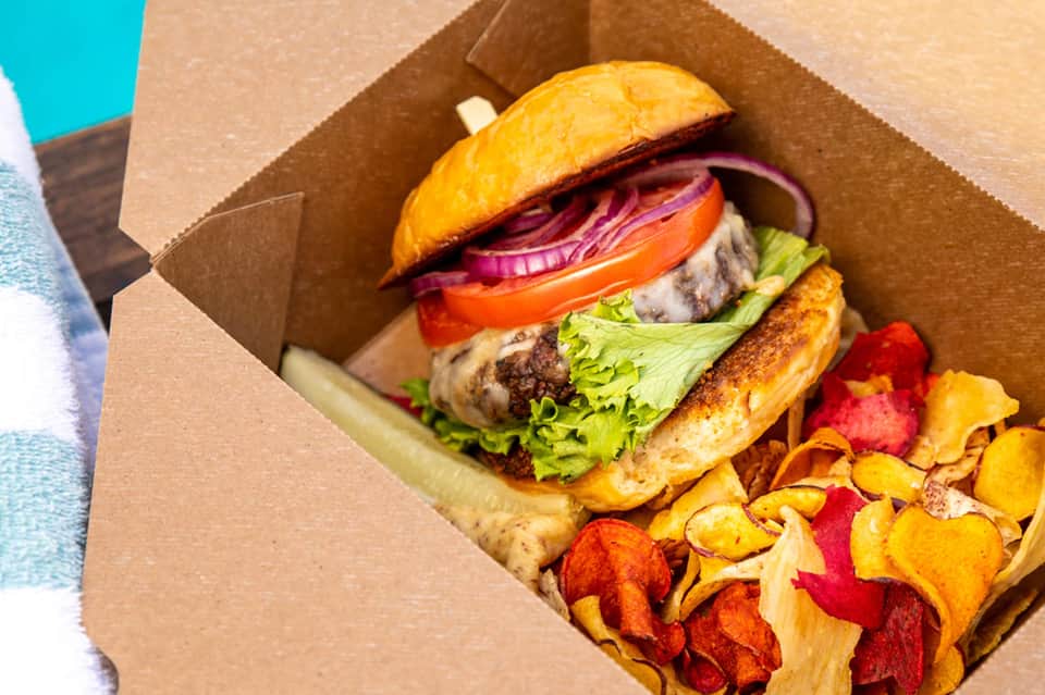 Gourmet burger with lettuce, tomato, and red onion in cardboard box with colorful vegetable chips