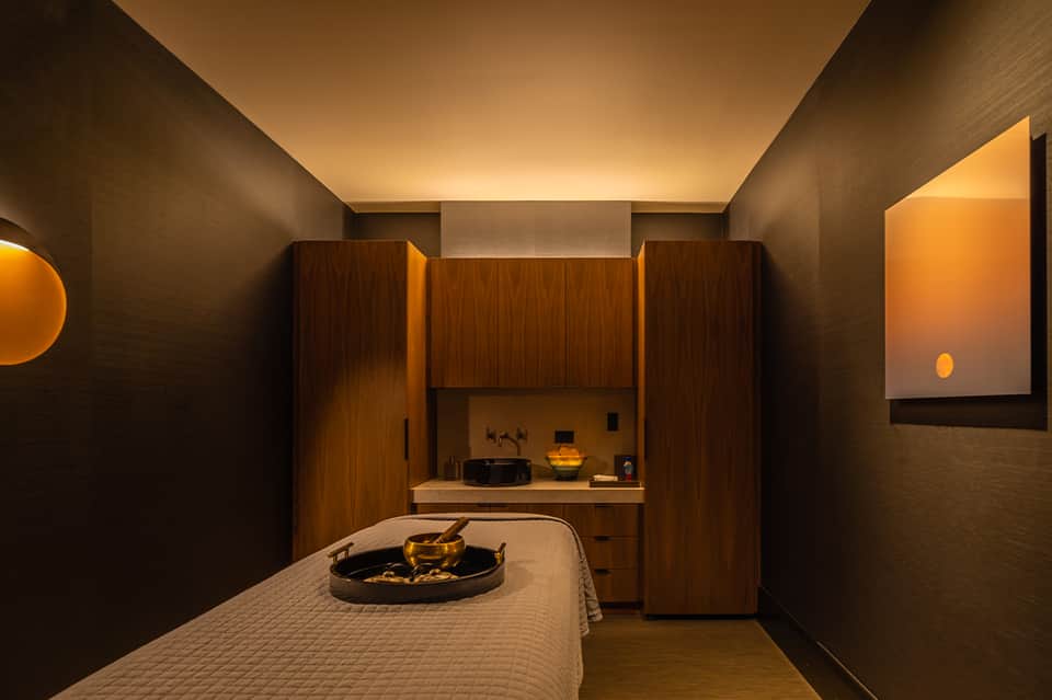 Spa treatment room with wooden cabinetry, warm lighting, and massage table with hot stones